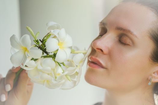 Close-up portrait of a woman holding white frangipani flowers with eyes closed, depicting serenity and natural beauty.