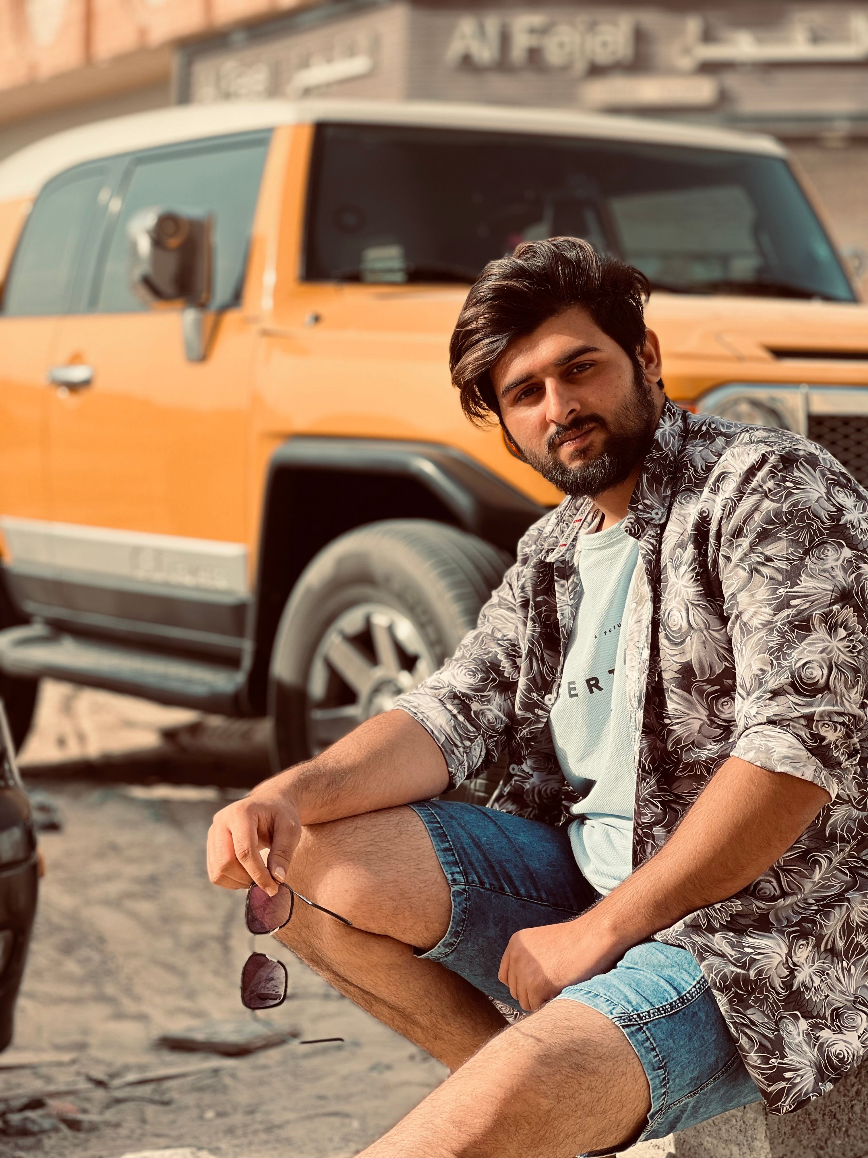 Young man in casual attire poses confidently beside a yellow SUV outdoors.