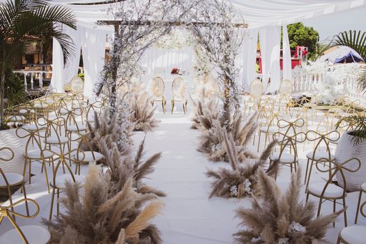 Elegant outdoor wedding setup in Angola featuring a white floral arch and golden chairs under a sunny sky.