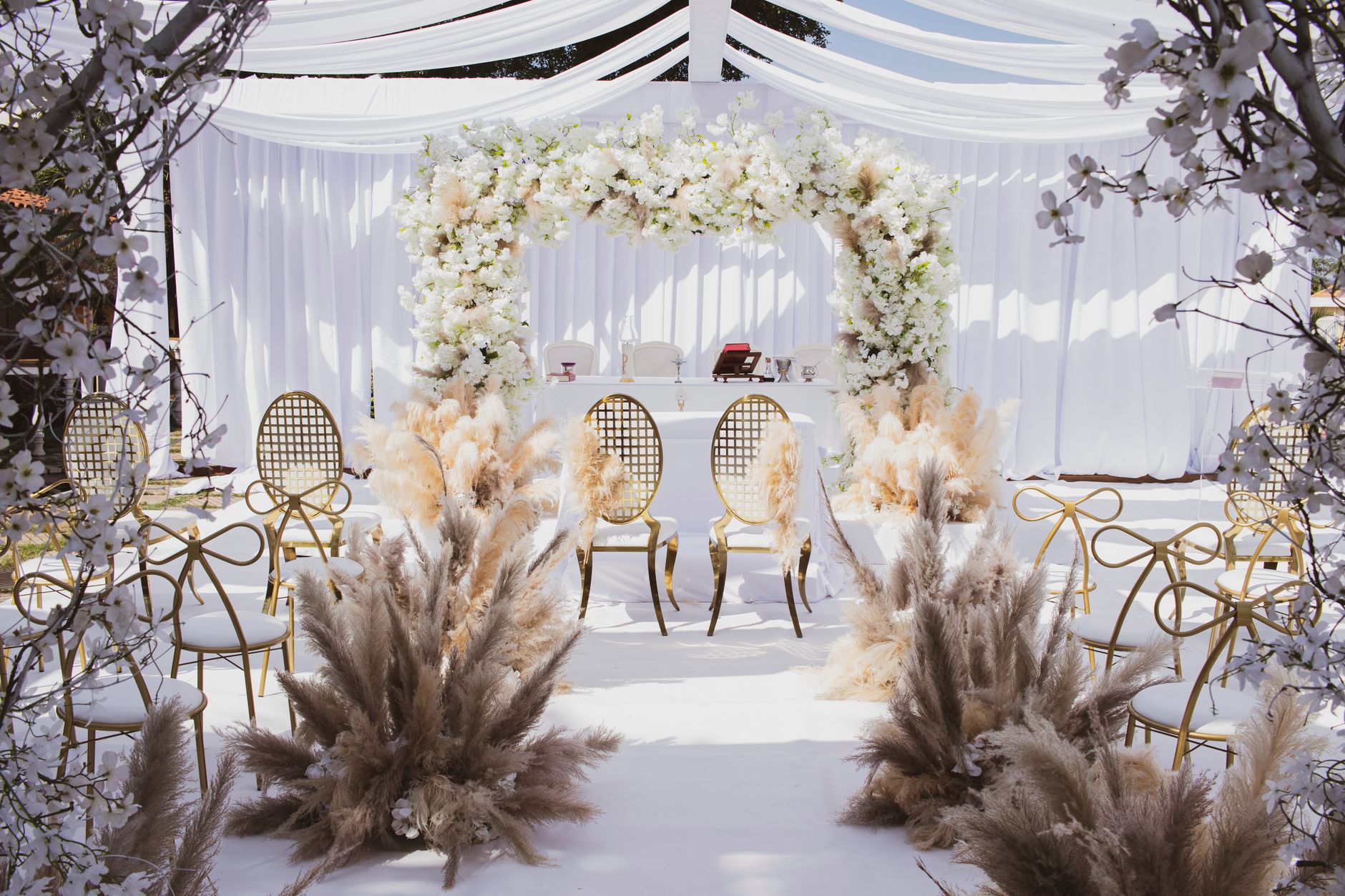 Beautifully decorated outdoor wedding setup with chairs and floral arch under a white canopy.