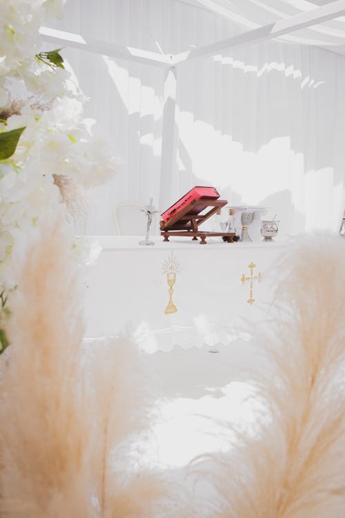 A Bible Beside a Cross on White Table Near White Flowers