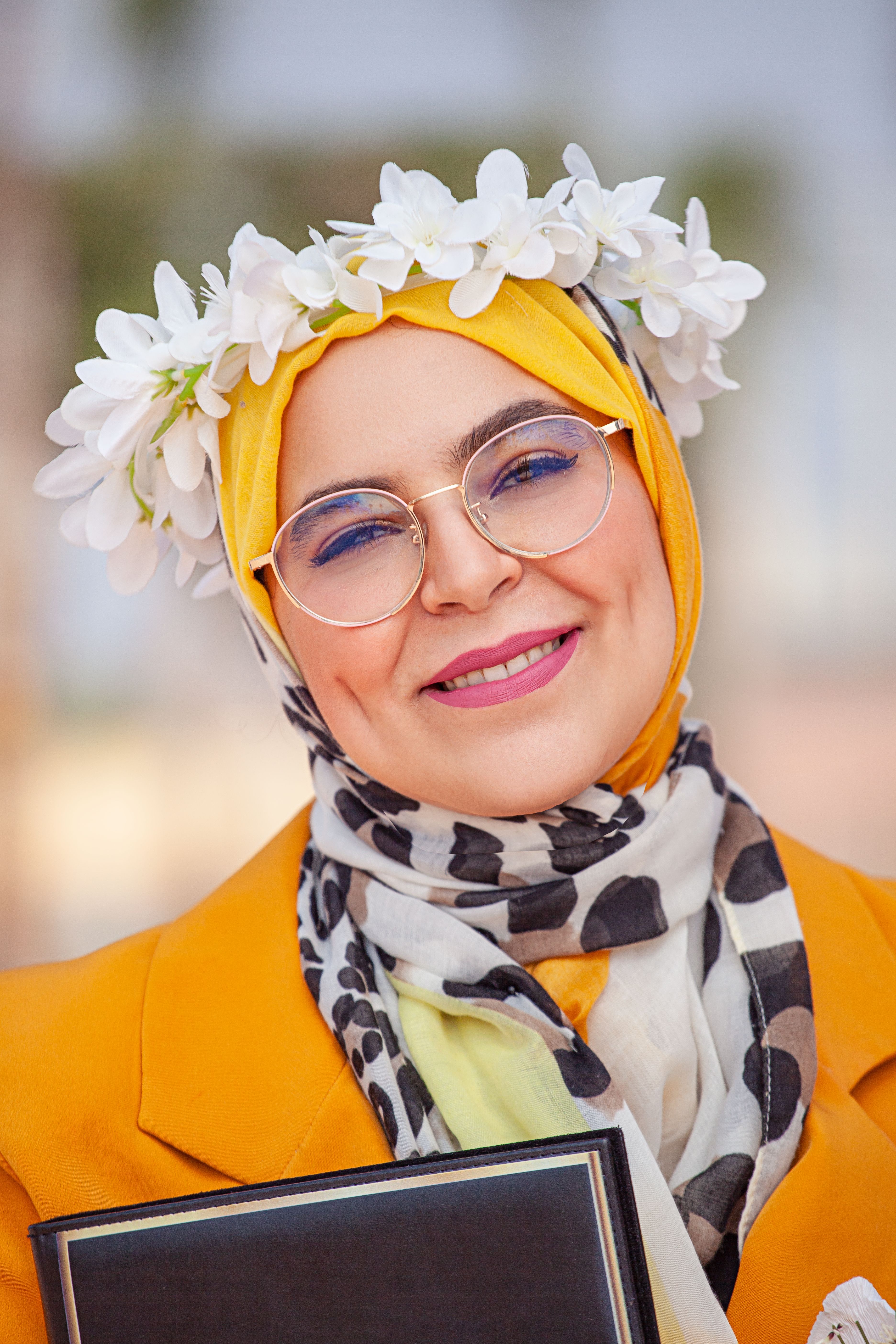 Smiling woman wearing hijab and glasses, adorned with a flower crown, captures an essence of joy and cultural beauty.