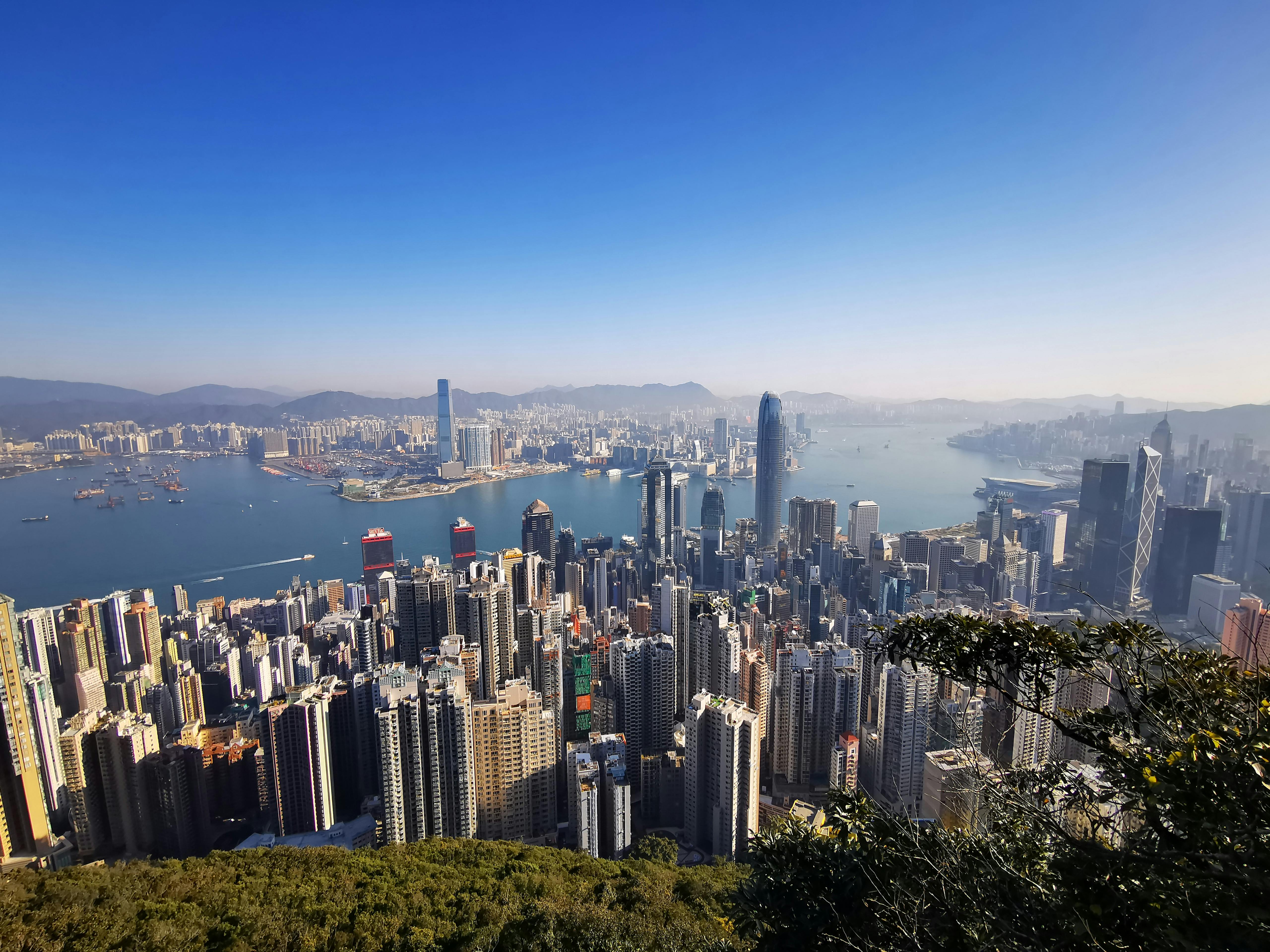 A breathtaking aerial view of Hong Kong's skyscraper-filled skyline and harbor under a clear blue sky.
