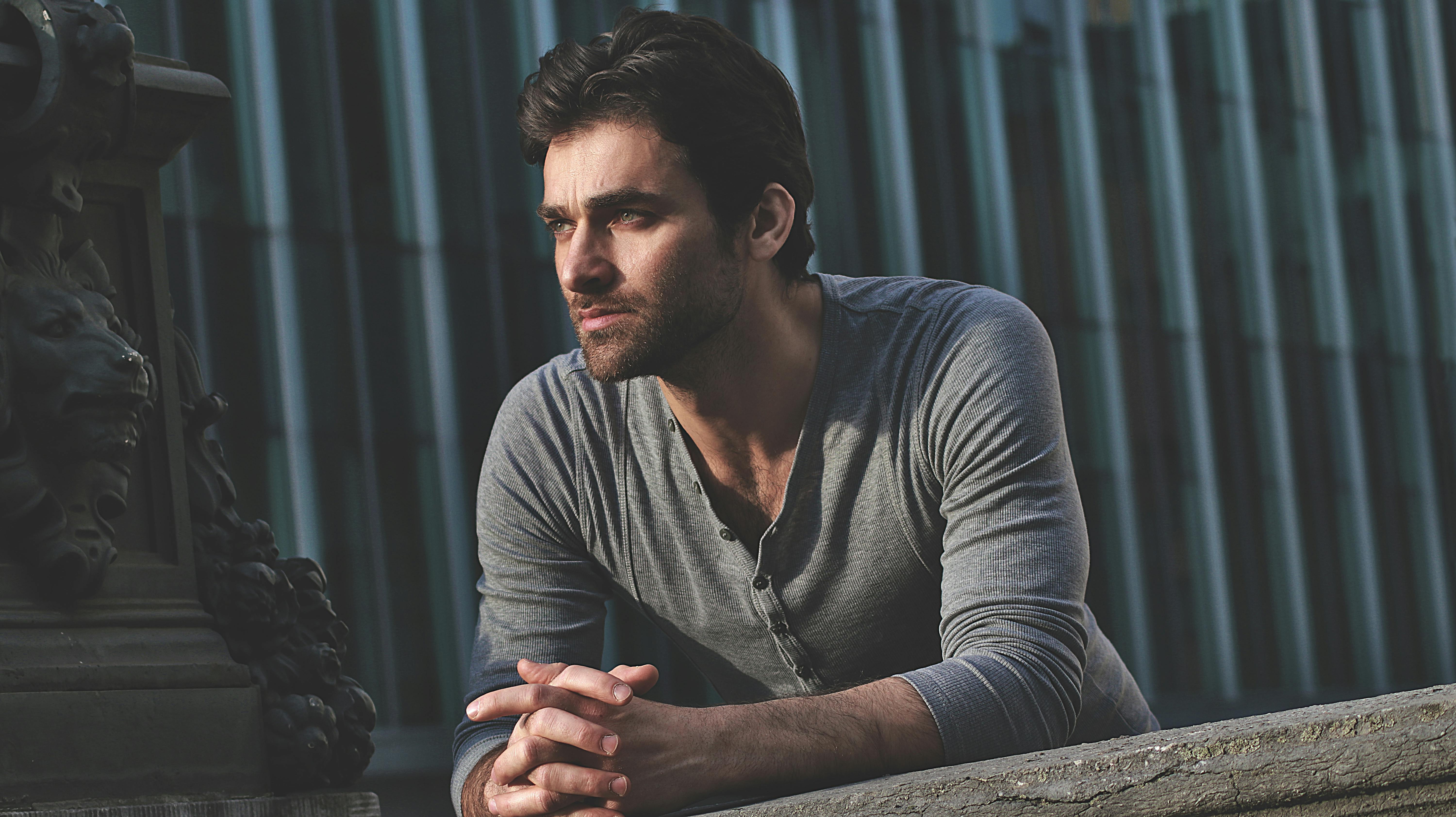 A serious man in gray long sleeves leaning on railing, looking afar with deep focus.