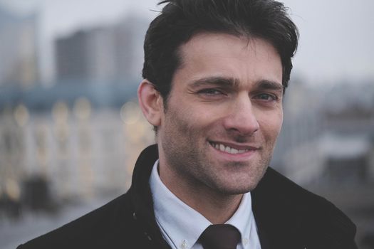 Close-up portrait of a confident man smiling outdoors in business attire.