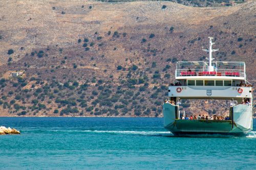 Free Ferry carrying passengers across the clear blue Ionian Sea in Greece, with rugged hills in the background. Stock Photo