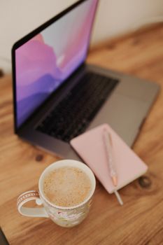 Warm workspace scene featuring a laptop, notebook, and coffee cup on a wooden desk.