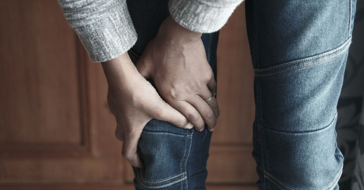 A person holds their knee in denim jeans, showing a sense of tension.