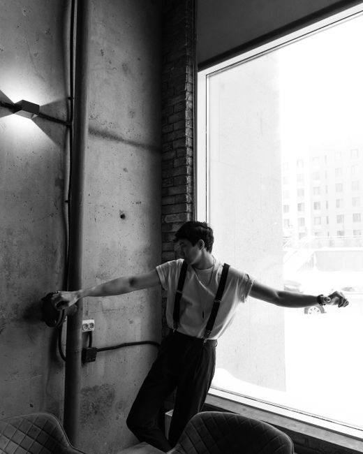 Black and white portrait of a man posing against a concrete wall in a modern indoor setting, Nur-Sultan.