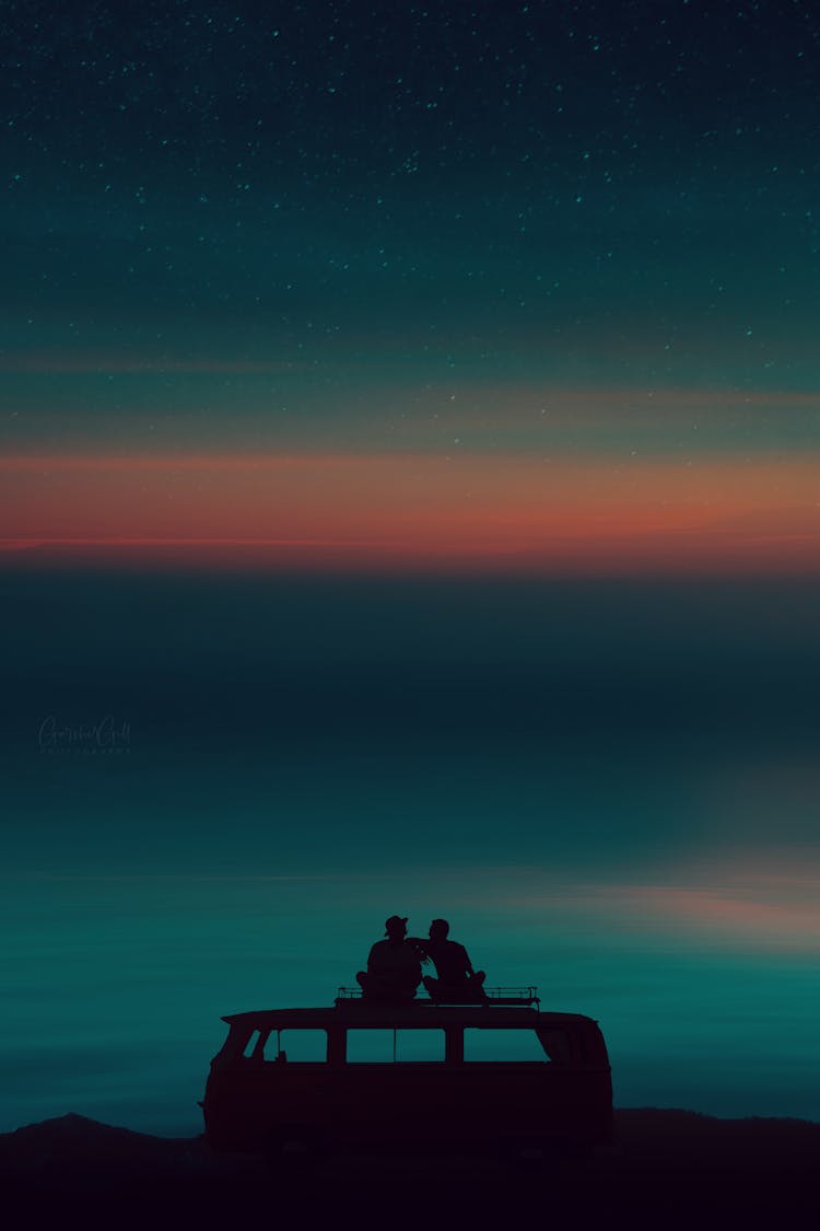 Silhouette Of People Sitting On The Roof Of A Campervan Under Evening Sky