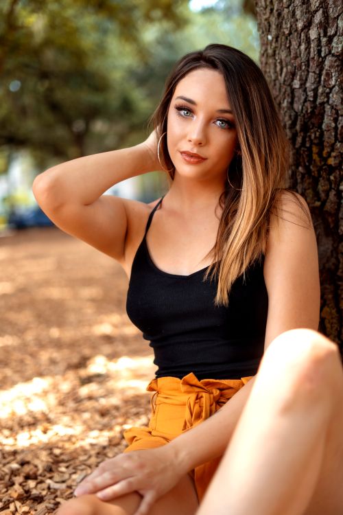 Free A stylish woman poses relaxed against a tree in an outdoor setting, showcasing fashion and elegance. Stock Photo