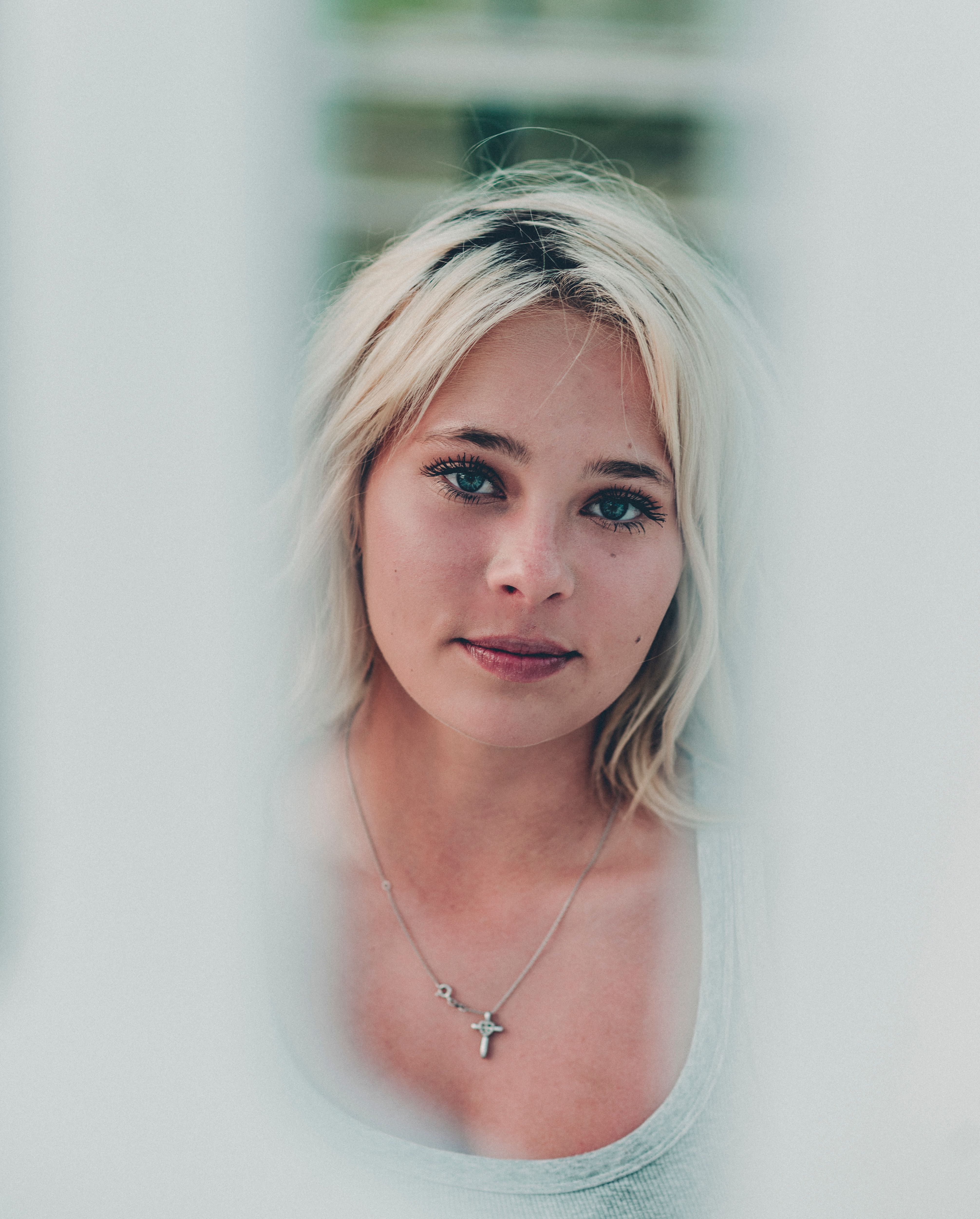 Portrait of a blonde woman with a necklace in soft focus outdoor setting.
