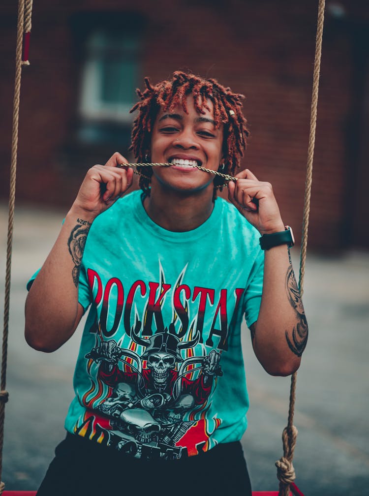 Teenager Wearing Turquoise T-Shirt With Graphics, Sitting On A Swing