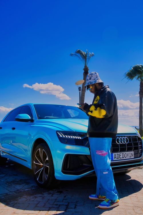 Free A man using his phone stands beside a blue Audi under a bright blue sky with palm trees. Stock Photo