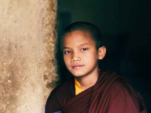 Free Young monk with a serene expression leaning against a textured wall. Stock Photo