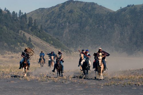 Free A group of horse riders galloping through a dusty field surrounded by hills. Stock Photo
