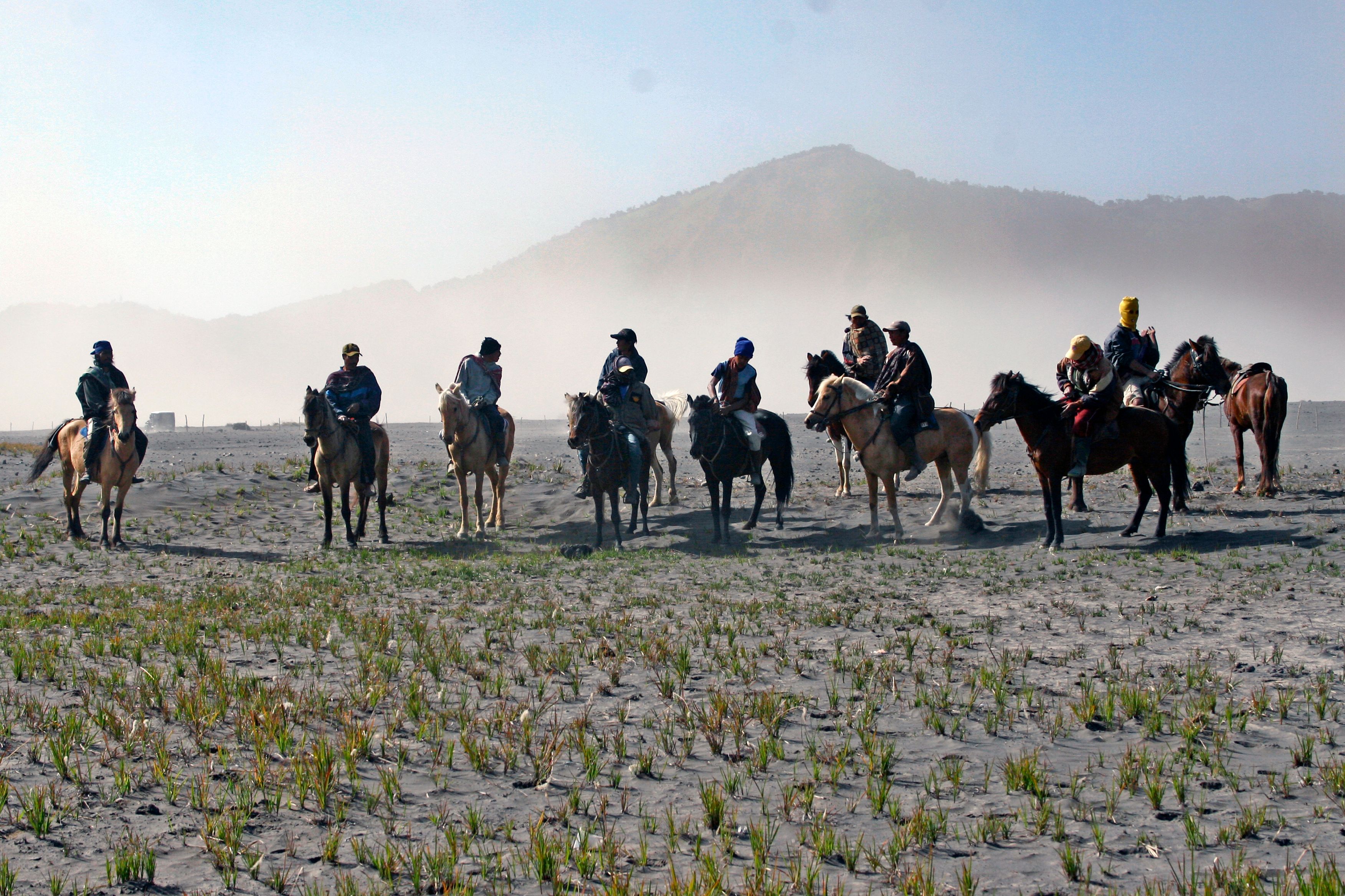 A group of people horseback riding on a misty field with mountains in the background.