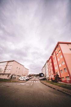 Low angle street view in Oleiros, featuring pastel buildings under a cloudy sky.