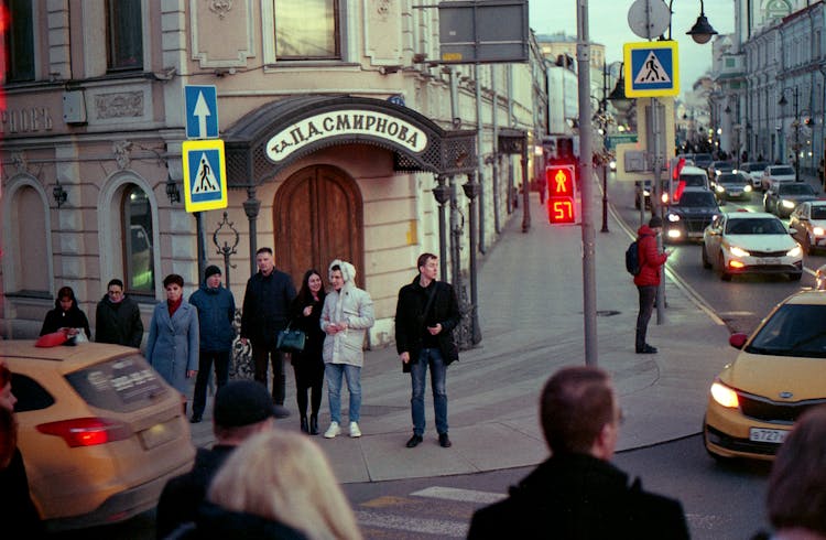 Busy People Standing On The Sidewalk While Walking On The Moving Cars On The Road