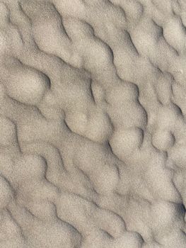 Detailed view of smooth, rippling sand texture resembling waves on a beach.