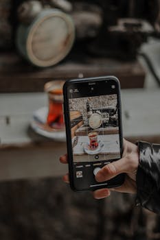 A close-up of a smartphone capturing a glass of tea on a table in a cozy rustic setting.
