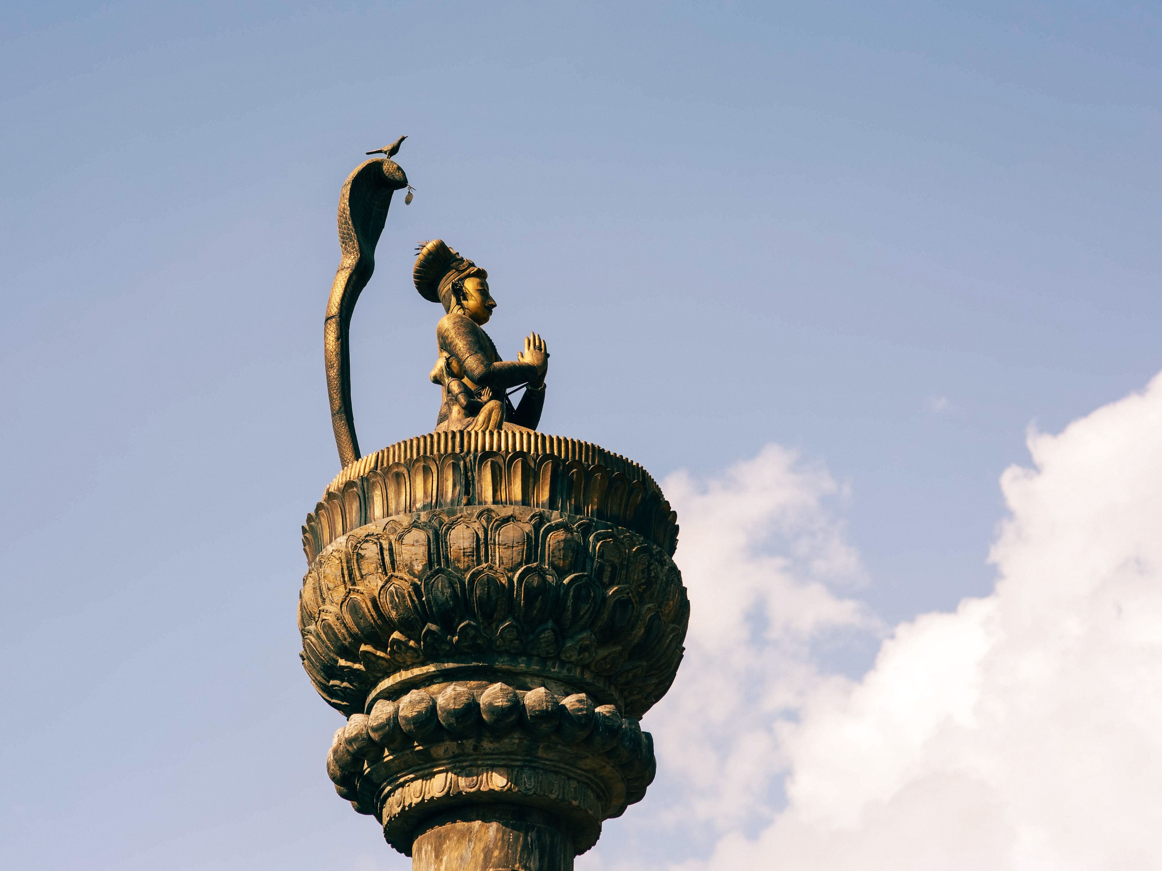 Low angle view of the Yoganarendra Malla statue with blue sky and clouds, showcasing cultural heritage.