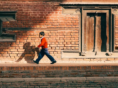 Boy Walking next to Brick Wall