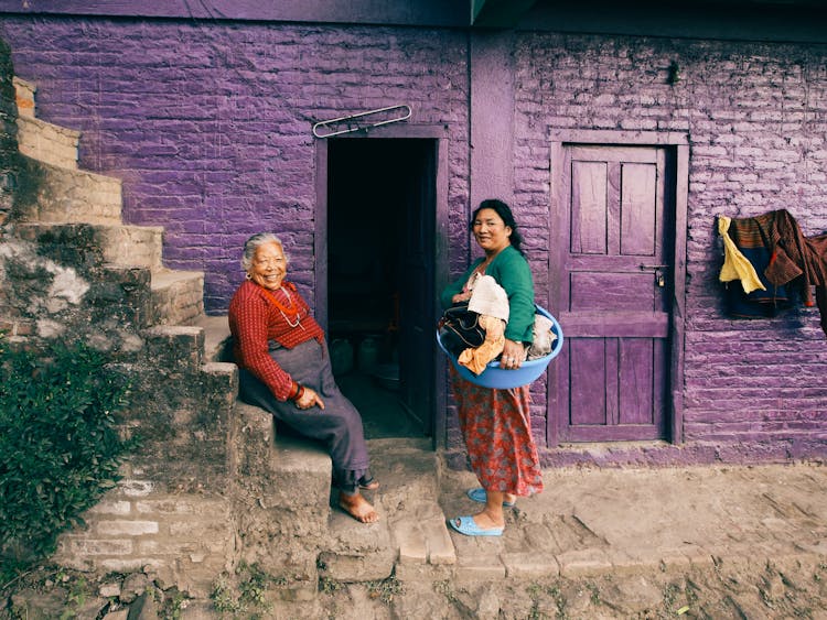 Woman Holding Laundry And Elderly Woman Sitting On Stairs