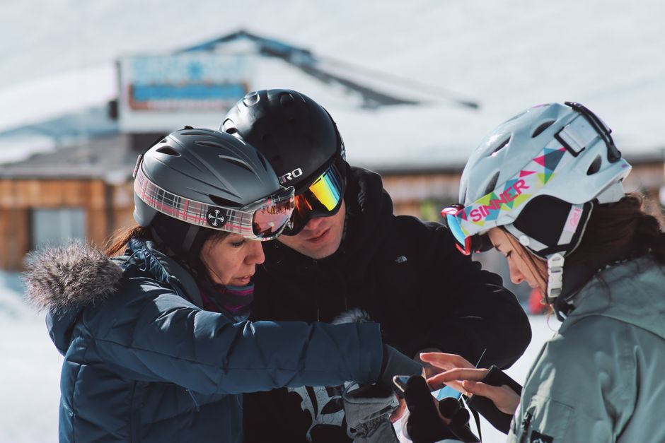 Three skiers interacting with a smartphone outdoors in Soelden, Austria during winter.