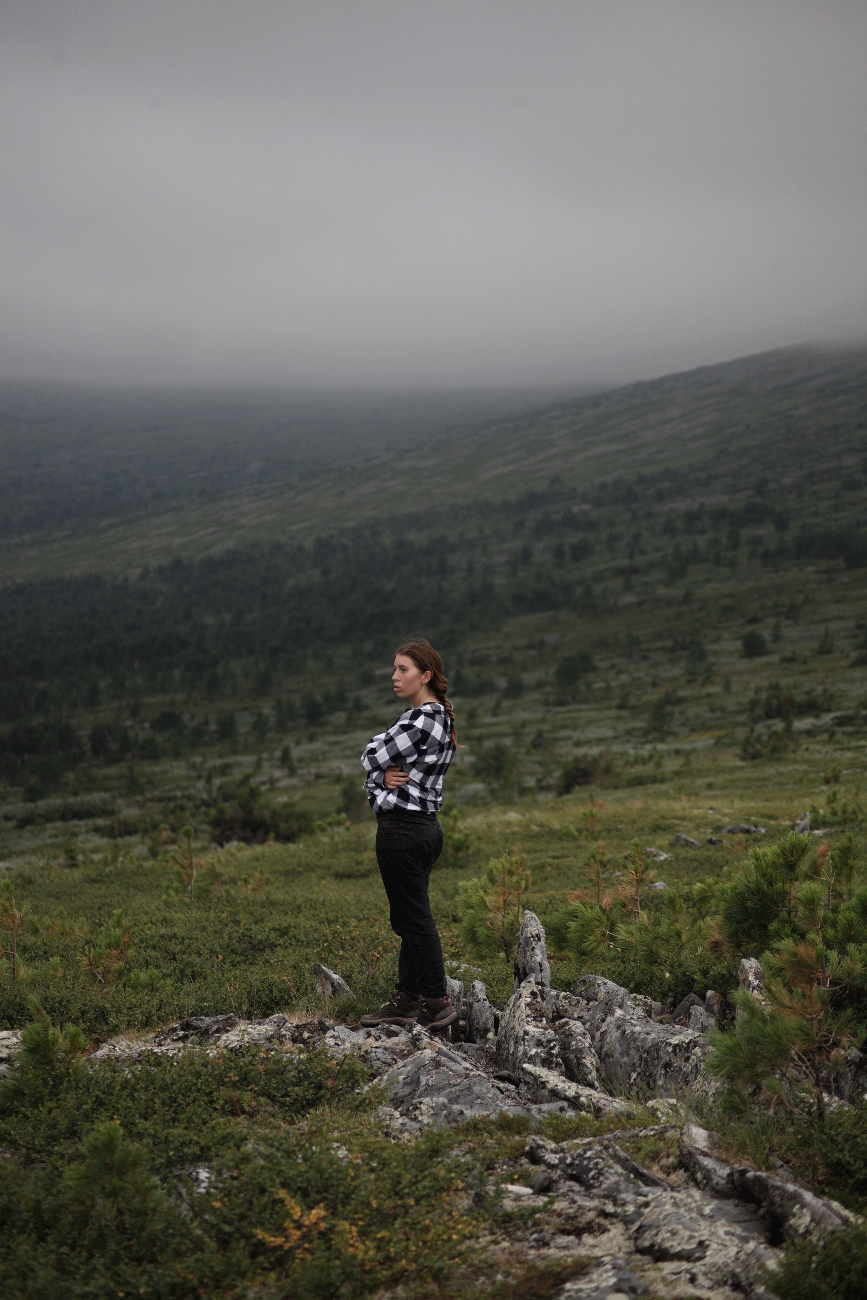 A woman stands on a rocky terrain, overlooking a misty, vast mountain landscape.