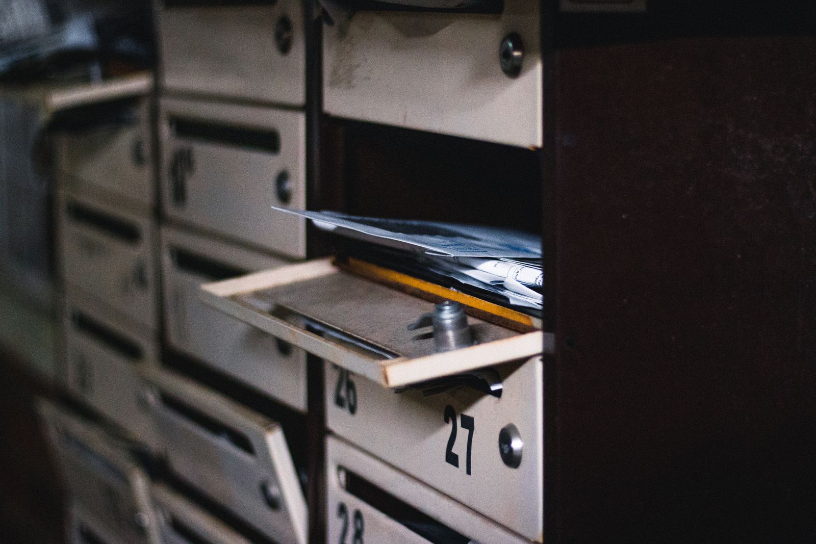 Rangée de boîtes aux lettres métalliques numérotées dans le hall d'un immeuble résidentiel, l'une d'elles ouverte et pleine de courrier