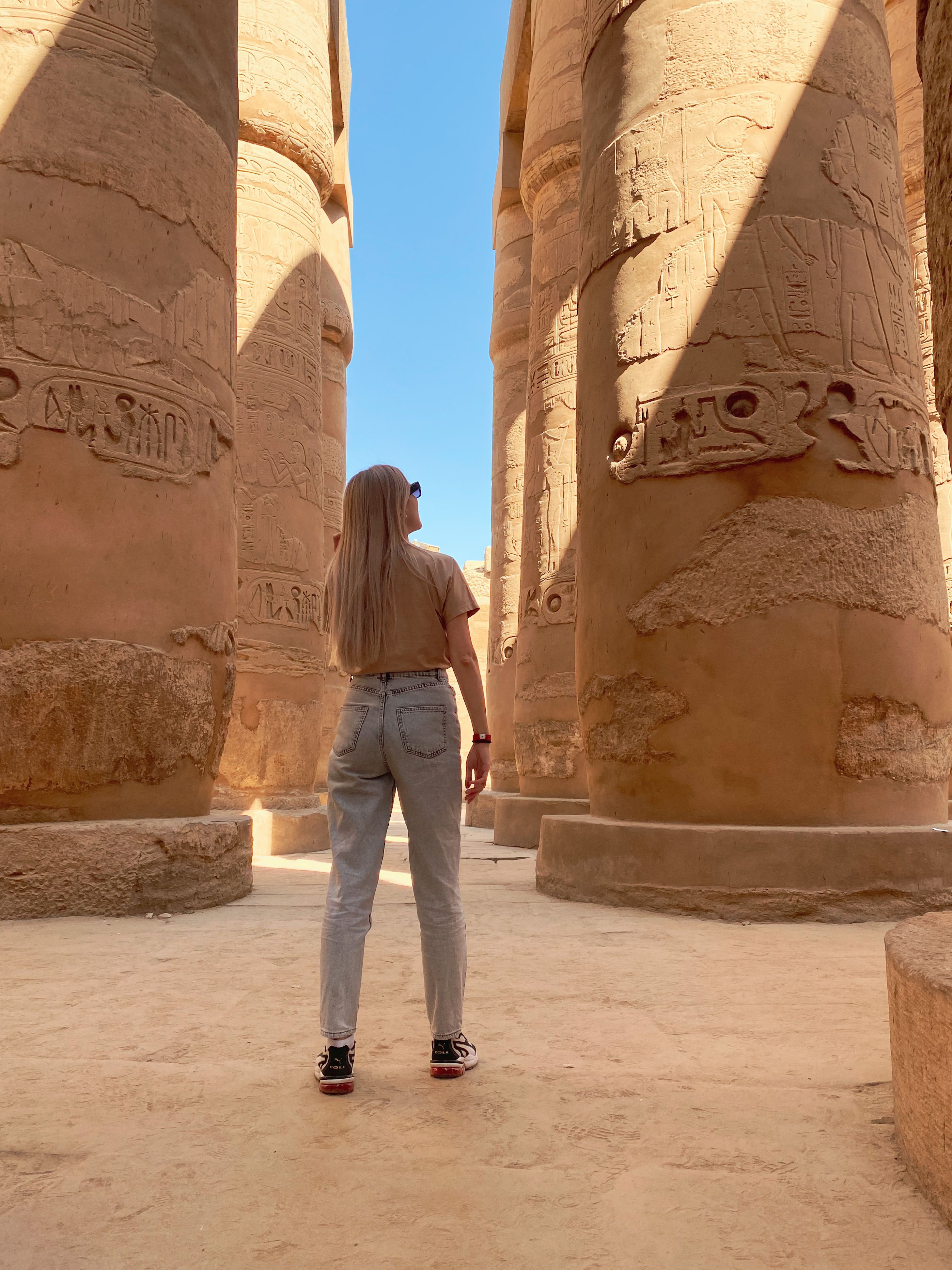 Tourist admires historic stone pillars at Karnak Temple, Luxor, Egypt.