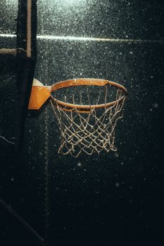 A lone basketball hoop dusted with snow captures the essence of outdoor winter sports at night.