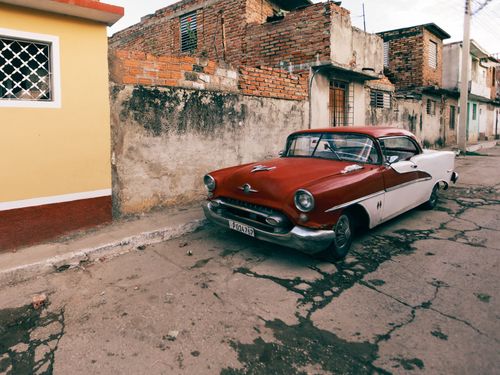 Free Classic red and white vintage car parked on a rustic street. Nostalgic and retro vibe. Stock Photo