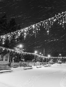 Snowy street adorned with twinkling string lights during a winter night, providing a festive ambiance.