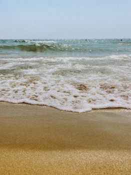 Peaceful sandy beach meeting gentle ocean waves under a clear sky.