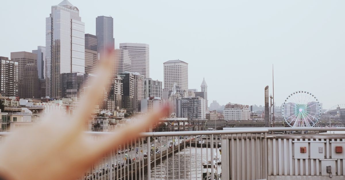 A vibrant Seattle skyline view featuring modern architecture and a Ferris wheel with a peace sign gesture in the foreground.