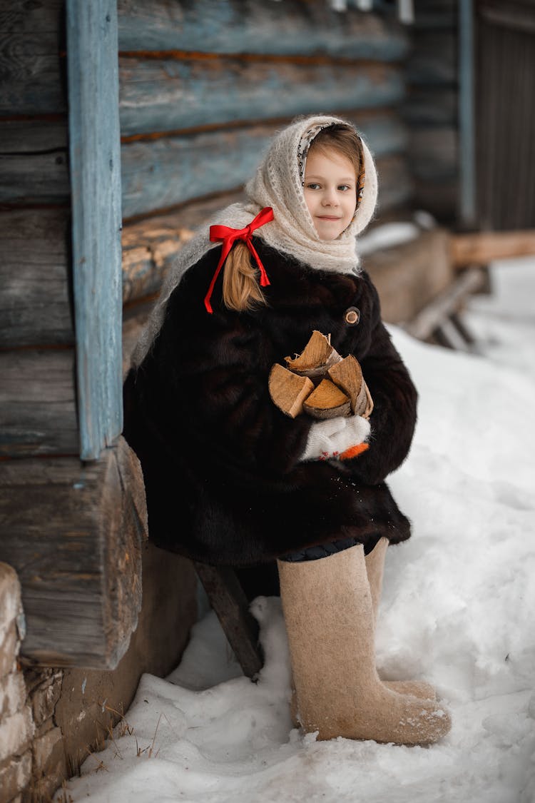 Girl In Winter Clothes Sitting On Bench Holding Wood