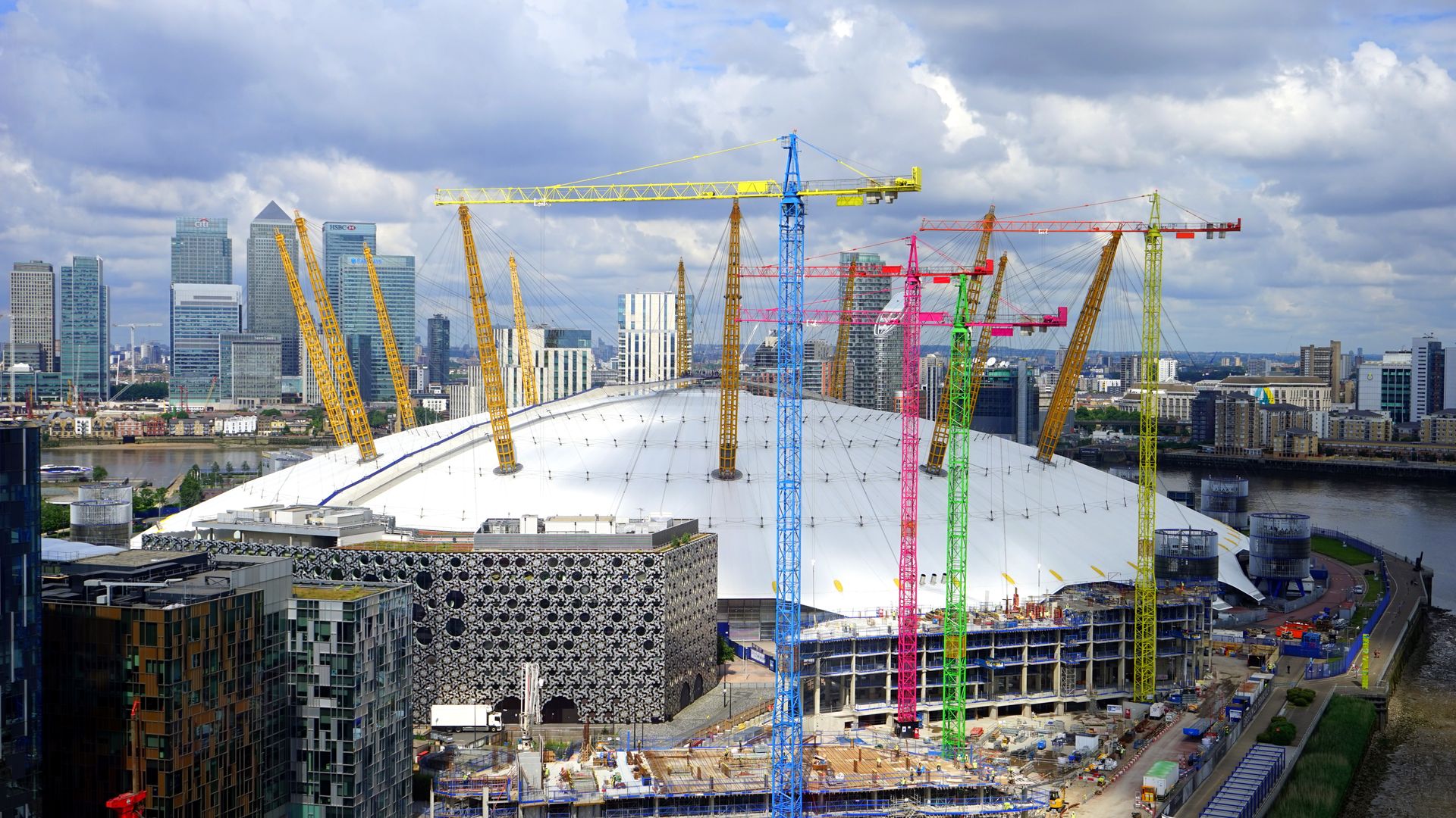 Aerial view of construction cranes and the O2 Stadium in London, showcasing urban development.