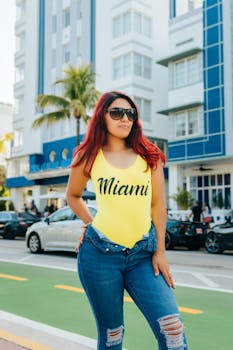 Woman in sunglasses poses confidently on Miami Beach street, wearing vibrant summer outfit.