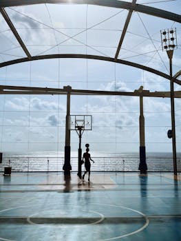 A silhouette of a basketball player shooting hoops on an outdoor court by the sea.
