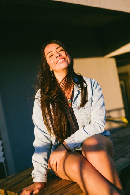 A woman with long brunette hair smiling while sitting outdoors in the golden hour light in Viña del Mar, Chile.