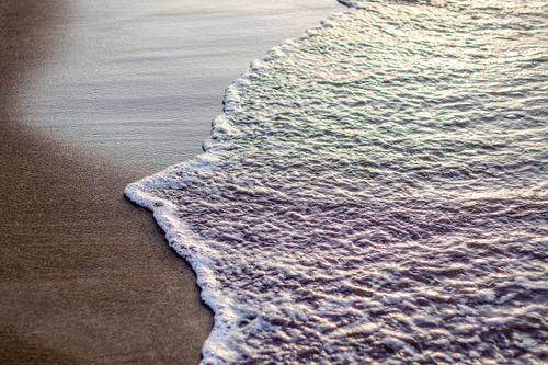 Free Close-up of gentle ocean wave lapping against smooth sandy beach under natural sunlight. Stock Photo