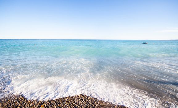 Peaceful beach scene in Nice, France, showcasing azure waves on a pebble shoreline with a clear sky.