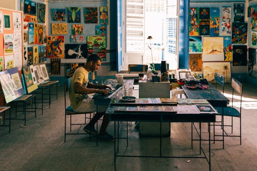 Artist working in a vibrant studio filled with colorful paintings and natural light.