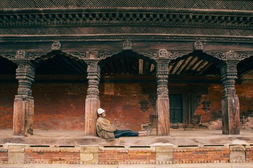 Free An elderly man sitting peacefully in a historic temple courtyard with ornate columns. Stock Photo