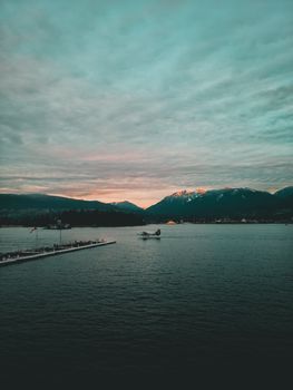 Seaplane over Vancouver's waterfront at twilight with mountain backdrop.