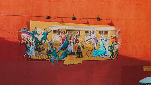 Free Street mural in Victoria, BC, depicting historical celebration and art on a red wall. Stock Photo