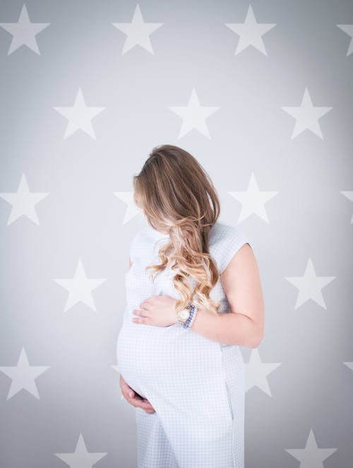 Free Pregnant Woman Wearing White Dress Holding Her Stomach Stock Photo