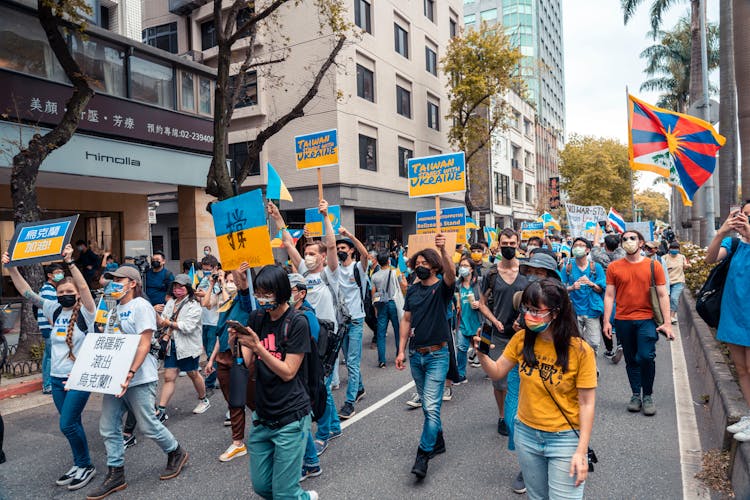 A Group Of People With Yellow And Blue Sign Boards Walking On A Street